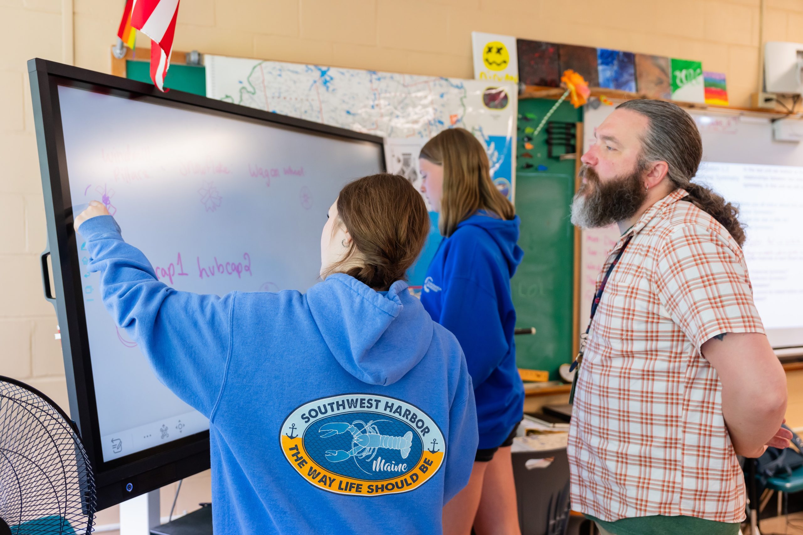 Teacher watching two students write on a smartboard